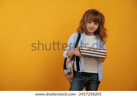 Holding books. Cute little girl is against yellow background.