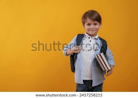 Ready for the school, holding books. Little boy is in the studio against yellow background.
