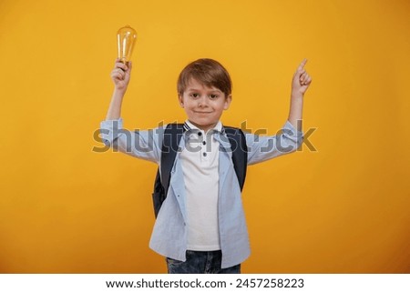 Light bulb in hand. Conception of smart person and idea. Little boy is in the studio against yellow background.