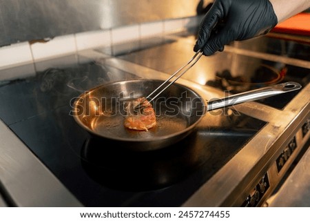 close-up on professional stove on a small frying pan the chef turns chicken fillet with tweezers