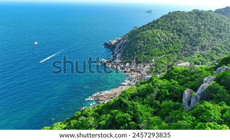 Boat meanders along rocky coast, embraced by verdant forest canopy. A picturesque vista from above. Drone aerial view. Cinematic footage. Tao island, Surat Thani, Southern Thailand. Beach background.
