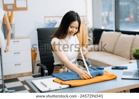 Successful fashion designer. Attractive young asian woman with smile while standing in workshop. Beautiful owner business woman working and holds tablet, laptop and smartphone 