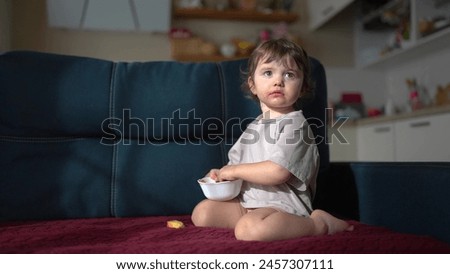 little child resting at home. happy and full of joy childhood, children's dream concept. a small girl are sitting on a blue sofa attentively watching cartoons on lifestyle TV and eat apples