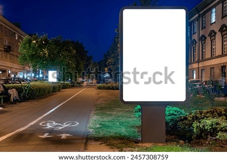 Blank White Billboard Mockup On Pedestrian Street Next To Bike Path At Night. Advertising Poster Lightbox For Commercial Branding