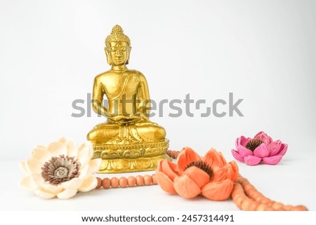 A golden statue of a Buddhist figure meditating wearing prayer beads decorate with flowers facing the front isolated on white background. Concept for Vesak Day and Enlightenment Day