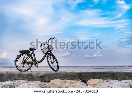 A Black bicycle parked on the sidewalk against a background of clouds and blue sky. In the photo there is negative space.