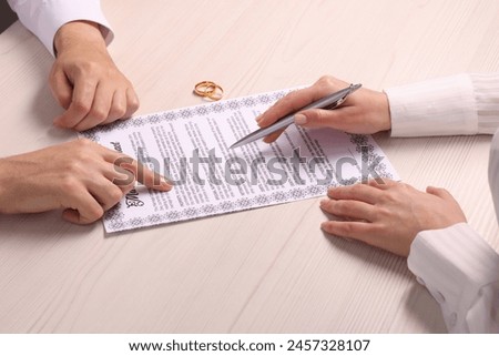 Man and woman signing marriage contract at light wooden table, closeup
