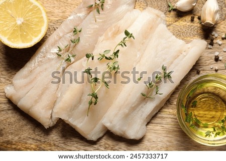 Raw cod fish, microgreens, lemon, oil and spices on wooden table, flat lay