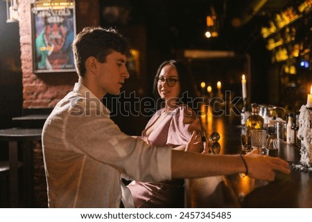 Female talk with new acquaintance near bar counter with bright picture on background. Evening by candlelight at bar with subdued light