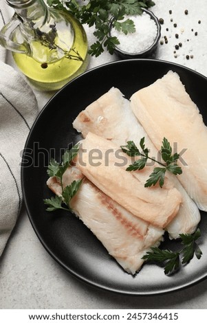 Plate with raw cod fish, parsley, oil and spices on light textured table, flat lay