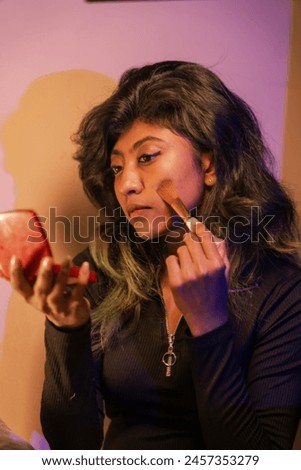 A woman is applying makeup in front of a mirror. She is using a red lipstick and a brush. Concept of self-care and confidence, as the woman takes the time to enhance her appearance