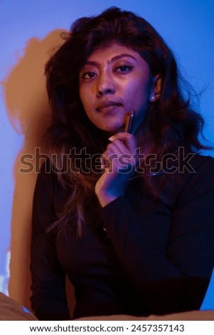 A woman with long hair is sitting on a bed and holding a pen in her hand. She is wearing a black dress and has a serious expression on her face. Concept of contemplation and introspection