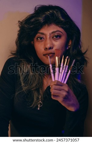 A woman is holding a brush set in her hand. She is wearing a black shirt and has green hair