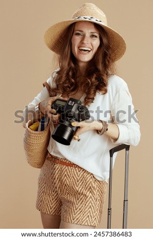 Beach vacation. happy stylish woman in white blouse and shorts on beige background with straw bag, trolley bag, photo camera and summer hat.