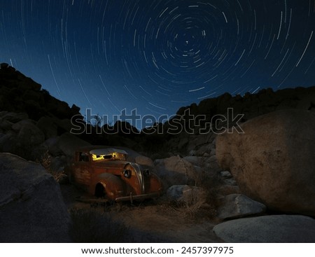 A vintage Hudson sits among the rocks of Joshua Tree National Park under a sky full of star trails.