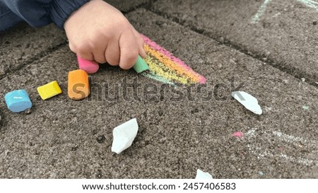 A child draws with chalk on the street. A rainbow pattern is drawn with multi-colored chalk on the asphalt on a sunny summer day. Creative development of children