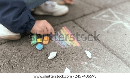 A child draws with chalk on the street. A rainbow pattern is drawn with multi-colored chalk on the asphalt on a sunny summer day. Creative development of children