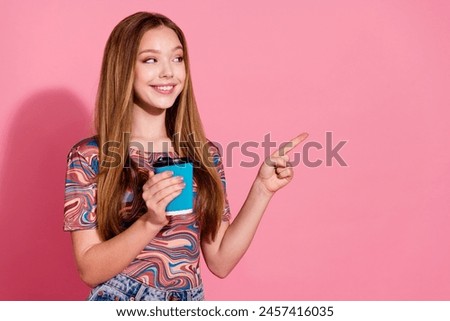 Photo of satisfied girl with straight hair holding cup of cappuccino look directing at promo empty space isolated on pink color background