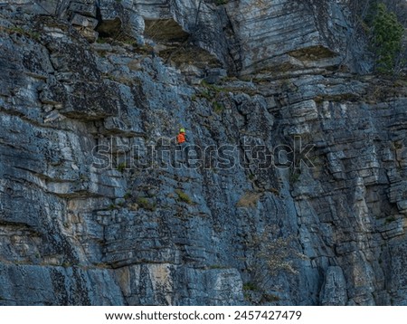 An aerial view of mountain climbers on the face of a cliff, enjoying their climb on a sunny day.