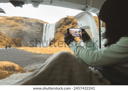 Traveler woman shoot video photo of beautiful waterfall use smartphone. Female tourist is taking photo with mobile phone camera while travel in Iceland stay in campervan by Skogafoss