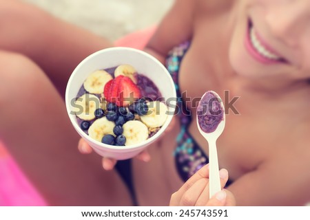 Acai bowl - girl eating healthy food on beach. Woman enjoying acai bowls made from acai berries and fruits outdoors on beach for breakfast. Girl on Hawaii eating local Hawaiian dish.