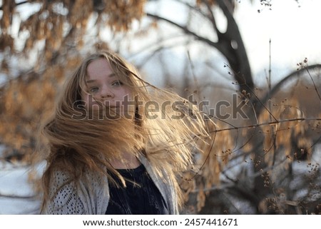 A blonde girl in a knitted sweater fools around and takes pictures in a winter park