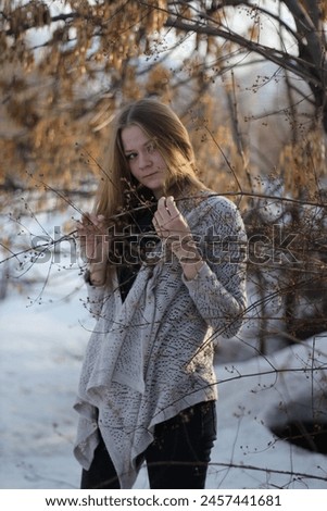 A blonde girl in a knitted sweater fools around and takes pictures in a winter park