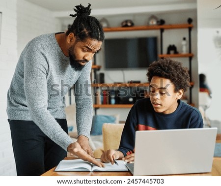 Father and son doing homework with laptop fighting and arguing over learning at home. Father and teenage son using laptop. Boy and dad sitting at home working with notebook, boy being bored 