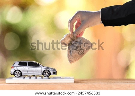 Business man hand hold the money bag present to the car put on the gold coin put on the wood in the public park, Loans for car concept.