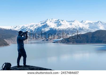 Hiker on W-trek hiking route on rock with camera towards Glacier Grey and Lago Grey Torres del Paine National Park, Chile during sunrise and in background snow covered mountains of Paine Massif