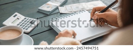 Business woman making entries in her notepad, coffee, calculator, money on the table, calculations. stock photo