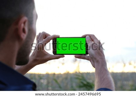 A man takes photos of nature at sunset with his mobile phone. Traveler man taking landscape photos on his green screen mobile phone