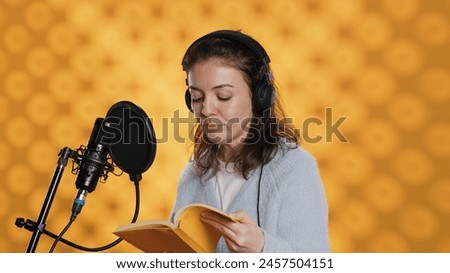 Influencer arriving in studio, putting headphones on, filming herself reading book with cellphone on tripod, creating audiobook. Woman doing vlog, recording novel using professional mic, camera A