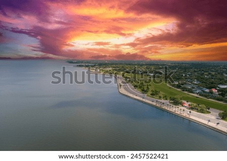 aerial shot along the coast of Lake Pontchartrain with homes, lush green trees, plants and grass, rippling water, powerful clouds at sunset in New Orleans Louisiana USA
