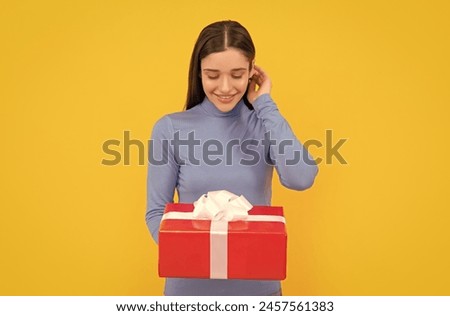 smiling girl holding gift box after shopping on yellow backdrop, purchase