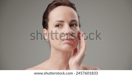 Beauty, health, cosmetics, anti-aging therapy and skin care concept - young beautiful brunette Caucasian woman touching face and looking at camera
