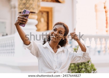 black girl selfie thumb up temple area smiling on vacation. female traveler in ancient religious landmark taking photo of self showing thumb. solo traveler girl enjoying taking selfie around location.