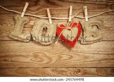 The Love word made of linen letters with a red textile heart on a rope on a vintage wooden background. St. Valentine's day concept. 