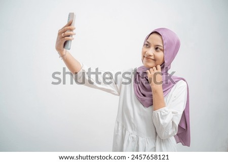 Cheerful young Muslim woman is posing gracefully with a happy and smiling expression, selfie shot on mobile phone in white background
