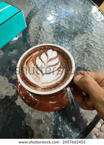 Photo of hot chocolate latte flavored drink held by an unidentified hand. The concept of a brown themed picture about food and drink.