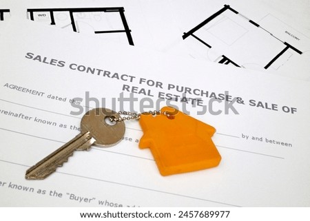 Close-up on a key attached to its key ring on the top of a sales contract for purchase  sale of real estate and building plans.