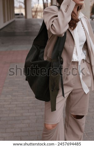 Expressing confidence and attitude. Beige suit and white blouse, female model posing holding on her shoulder green trendy big bag, urban background, sun glasses. Fashion lifestyle cropped image