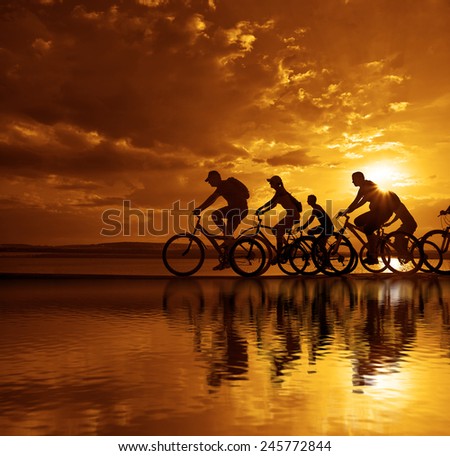 Image of sporty company friends on bicycles outdoors against sunset. Silhouette A lot phases of motion go of six 6 cyclist along shoreline coast Reflection sun on water Copy Space for inscription