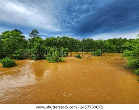 This is a landscape picture of a field that has been flooded during a severe storm. This picture has trees under water in the foreground and dark, gloomy clouds in the background.