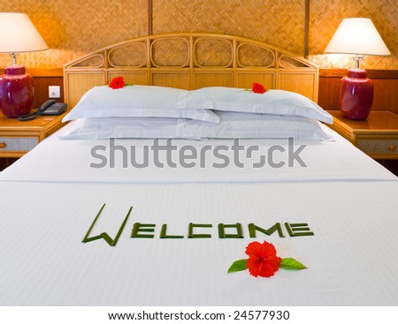 Word Welcome made of palm leafs and flowers on bed