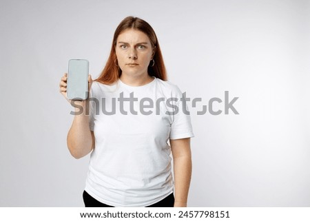 Sad angry 30s woman with blank screen mobile phone on white background, studio portrait.