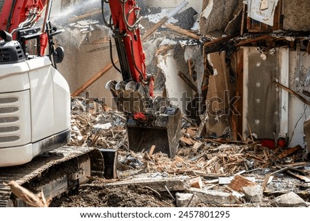 Demolishing an old home in a residential neighborhood to clear a lot and make way for a new home, heavy equipment with jawbone bucket to rip apart structure. Royalty-Free Stock Photo #2457801295