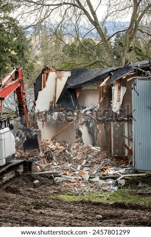 Demolishing an old home in a residential neighborhood to clear a lot and make way for a new home, heavy equipment with jawbone bucket to rip apart structure.
 Royalty-Free Stock Photo #2457801299