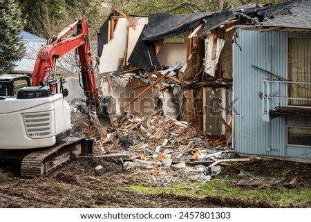 Demolishing an old home in a residential neighborhood to clear a lot and make way for a new home, heavy equipment with jawbone bucket to rip apart structure.
 Royalty-Free Stock Photo #2457801303
