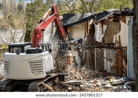 Demolishing an old home in a residential neighborhood to clear a lot and make way for a new home, heavy equipment with jawbone bucket to rip apart structure.
 Royalty-Free Stock Photo #2457801317